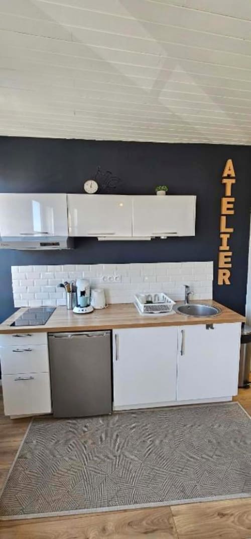 Cuisine moderne de l'appartement L'Atelier aux Gîtes Saint Valery En Caux avec armoires blanches, plan de travail en bois et acier inoxydable