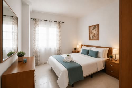Chambre lumineuse de Sara & Gino Fuerteventura avec mobilier en bois, literie blanche, accents bleu-vert et fenêtres avec lumière naturelle