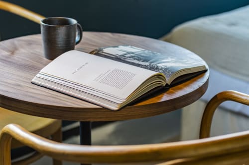 Livro aberto e caneca metálica sobre mesa redonda de madeira em estúdio de hotel no Porto com vista da cidade