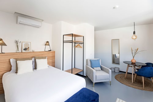 Estúdio moderno no Porto com cama branca, cabeceira de madeira, detalhes azuis, área de estar e planta aberta