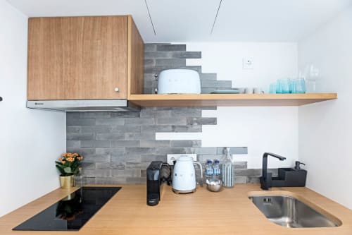 Kitchenette moderna em quarto do hotel Benefit Collection, Porto, com armários de madeira, painel de azulejos cinza e aço inoxidável