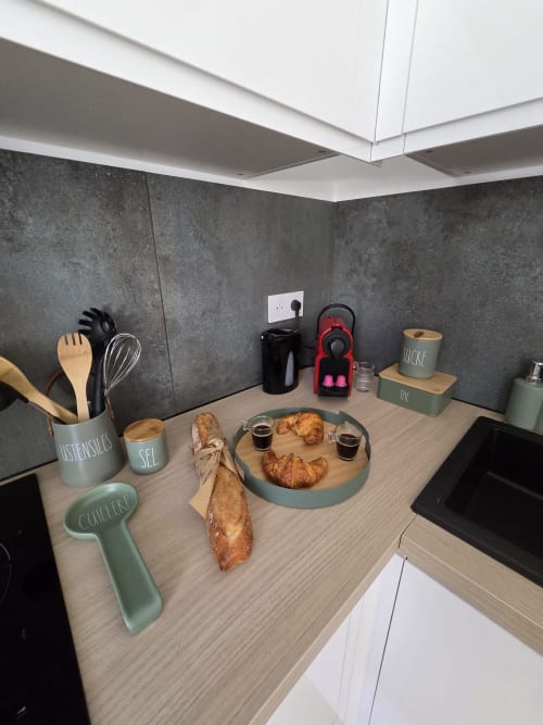 Comptoir de cuisine moderne à la Résidence Cosy avec croissants, pain, tasses de café et éléments de décoration française sur surface en bois