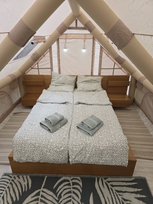 Chambre douillette dans une tente de glamping au Domaine Trianon avec lit en bois, literie à motifs et toiles de coton