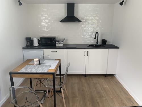 Cuisine et salle à manger modernes du gîte d'Étretat avec plan de travail noir, armoires blanches et table en bois.