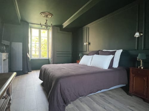 Chambre élégante à La Millière avec murs vert sauge, lit queen avec oreillers blancs, table de nuit en bois, lustre et jardin