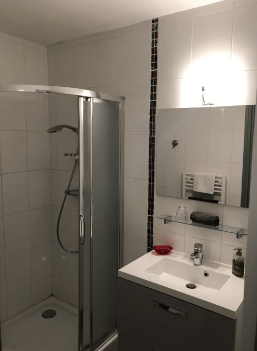 Salle de bain moderne de l'appartement Le Paillot de Montabert à Troyes, avec douche, lavabo, miroir et carrelage blanc