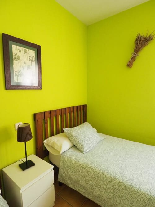 Dormitorio verde lima brillante con cama de madera, mesita de noche blanca, lámpara de escritorio y cuadro de mariposa enmarcado en Rural Senda del