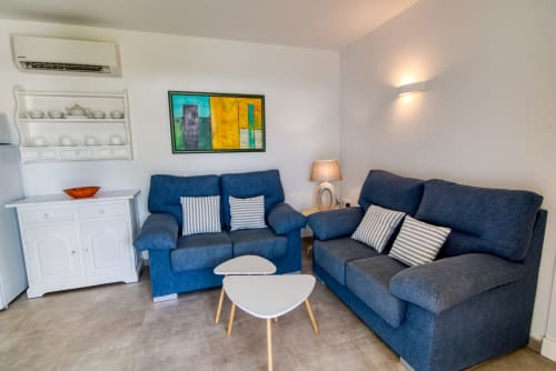 Sala de estar moderna con sofás azules, muebles blancos y arte colorido en Las Golondrinas, Cap d'Artrutx