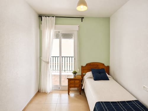 Habitación individual en Apartamentos El Calón Playa con cama de madera, acceso a balcón y pared de acento verde claro