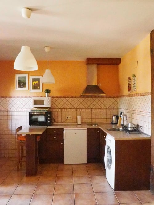 Cocina con paredes naranjas, armarios de madera oscura y piso de baldosa beige en Apartamentos Senda del Duratón, Sebúlcor