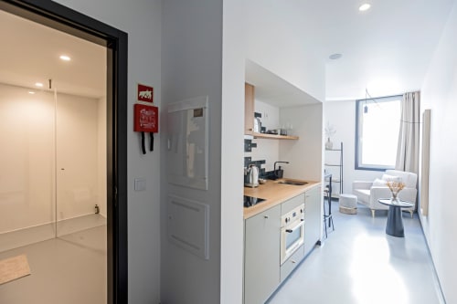 Moderno estúdio de hotel no Porto com kitchenete, móveis brancos, bancada de madeira, sala de estar e banheiro