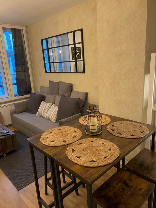 Salon moderne avec table à manger, canapé gris et vue sur la ville à l'hôtel Le Paillot de Montabert à Troyes