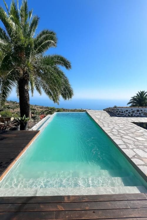 Piscina infinita turquesa con vistas al océano en villa Nexus, Tijarafe, La Palma, rodeada de palmeras bajo un cielo azul