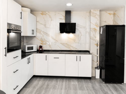 Cocina moderna en Apartamento Lateral Perla con muebles blancos, encimeras negras, backsplash de mármol y acero inoxidable