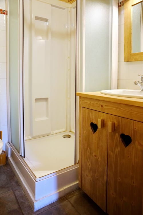 Modern bathroom with walk-in shower, wooden vanity with heart cutouts, and white tile walls at Chalet La Louvière