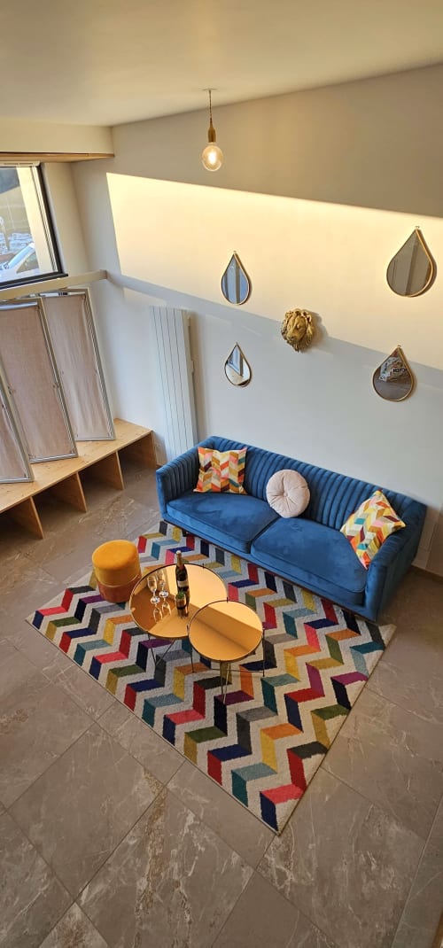 Salon loft contemporain aux Gites Saint Valery En Caux avec canapé bleu velours, tapis géométrique coloré et miroirs gouttes sur le mur
