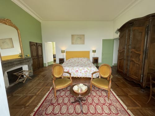 Élégante chambre au Château de Vaux Morvan avec cheminée, tête de lit jaune, meubles anciens et vue sur les jardins