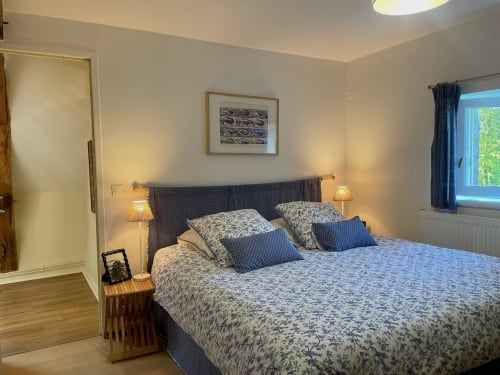 Chambre lumineuse au Château de Vaux Morvan avec lit queen-size, literie bleue à motifs, lampes de chevet et vue sur le jardin