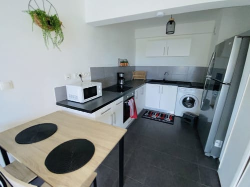 Cuisine moderne à Cayenne : comptoirs noirs, armoires blanches, électroménagers inox et table en bois