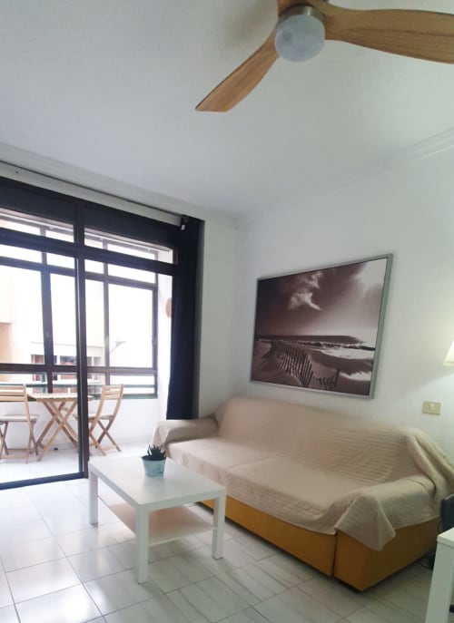 Luminoso soggiorno al Medano Center con divano color crema, tavolino bianco, TV a parete, ventilatore da soffitto e balcone