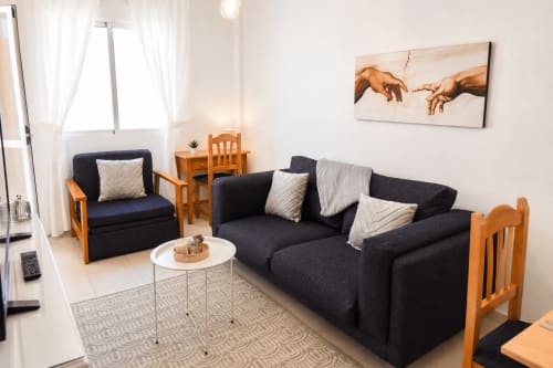 Moderno salón con sofá oscuro, sillas de madera y obra contemporánea en Apartamentos El Calón Playa, Cuevas