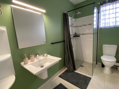Salle de bains moderne et verdoyante avec lavabo blanc, miroir, douche pluie et toilettes à l'appartement Kay Betty en Martinique