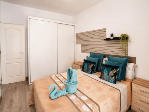 Moderno dormitorio en Apartamentos El Calón Playa con cabecera de lamas de madera, almohadas turquesas y decoración temática marina en Cuevas del