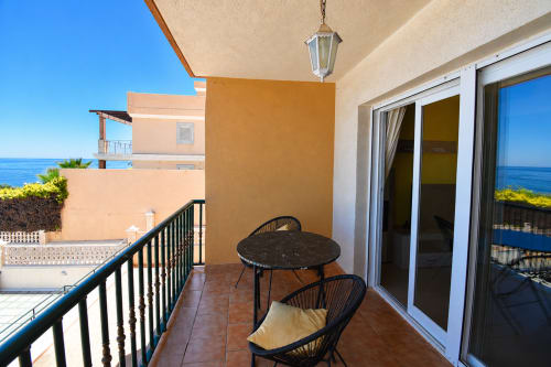 Terraza de apartamento frente al mar con vistas al océano, sillas y mesa negras, puertas de cristal hacia el interior