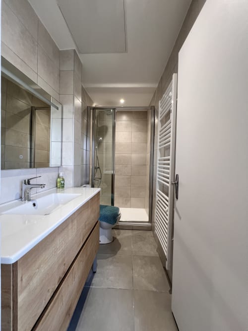 Salle de bains moderne avec meuble-lavabo en bois, cabine de douche et sèche-serviettes électrique au gîte Le Restaurant du Port à Saint Pierre de