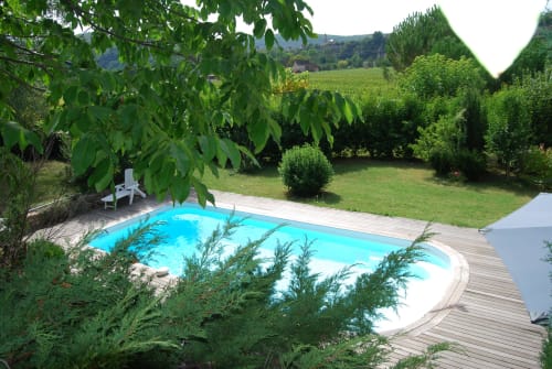 Piscine turquoise avec terrasse en bois entourée de jardins luxuriants aux Pratges, Figeac