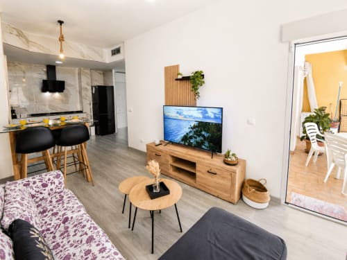 Moderna sala de estar en El Calón Playa con mueble de TV en madera, sofá, cocina y acceso a balcón en Cuevas del