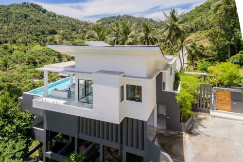 Modern white villa with infinity pool surrounded by lush tropical jungle hills in Ko Samui, Thailand