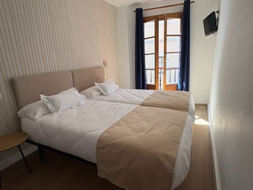 Habitación doble de la Pensión Argüelles en Ribadesella con dos camas, balcón con vistas a la ciudad y TV de pantalla plana