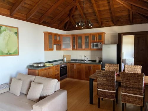 Zona de estar abierta de Villa Awara con cocina de madera, mesa de comedor, sofá y vigas vistas en El Pinillo