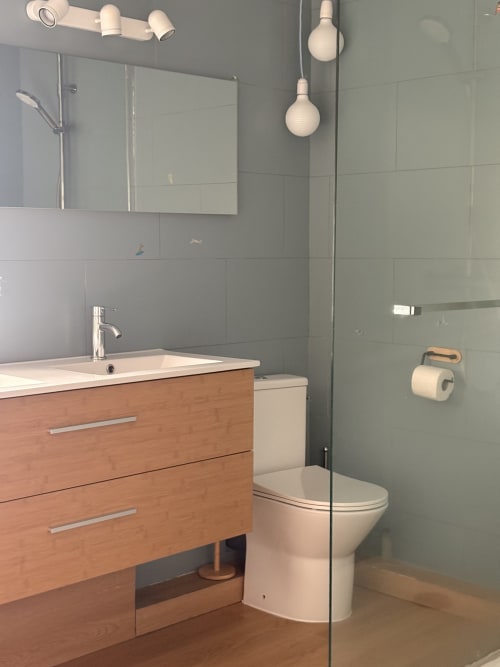Salle de bain moderne à La Villa Maraloupia avec meuble vasque en bois, carrelage gris, douche vitrée et luminaires contemporains
