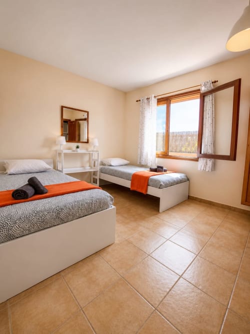 Luminoso dormitorio doble en villa Sara & Gino Fuerteventura con camas blancas, detalles naranjas, ventanas de madera y baldosas de terracota