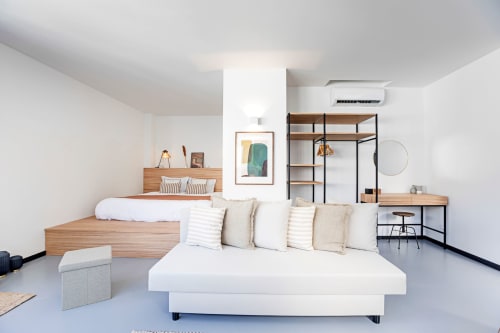 Moderno apartamento estúdio no Porto com sofá branco, cama de madeira, prateleiras, mesa de trabalho e móveis contemporâneos