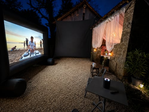 Installation de cinéma en plein air au Domaine Valenquercy avec écran privé, salon confortable et bâtiment en pierre illuminé