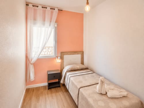 Single bed bedroom with coral accent wall and sea view window at Apartamentos El Calón Playa, Cuevas del Almanzora