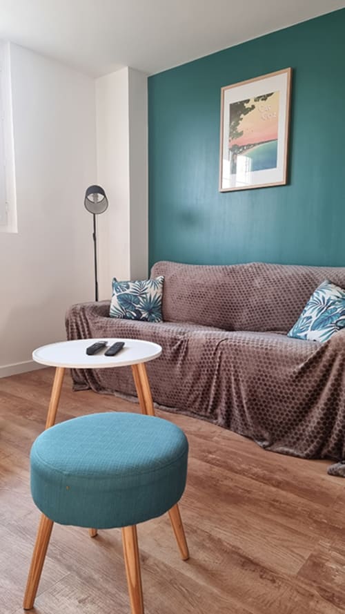Modern sitting area in Ô LOCH apartment with teal accent wall, gray sofa, round side table, and teal ottoman at Location
