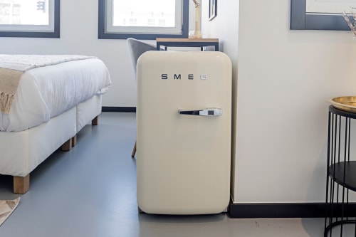 Refrigerador SMEG creme no estúdio compacto Porto da Coleção Benefit, com cama e decoração moderna visível