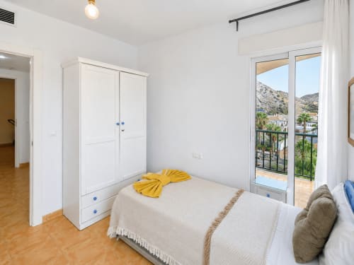 Bright bedroom at Apartamentos El Calón Playa with white wardrobe, sea view balcony, and terracotta tile flooring