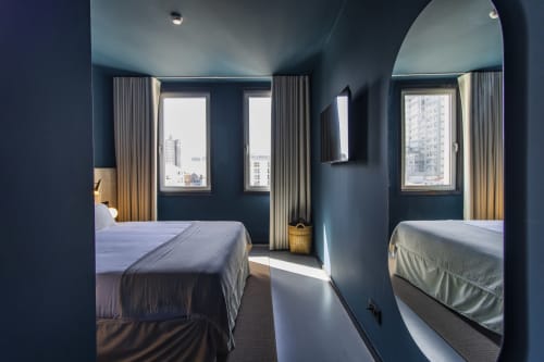 Modern Porto hotel bedroom with dark blue walls, two beds, large windows, city views, and contemporary furnishings.