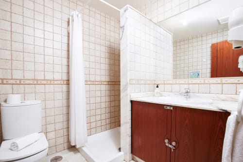 Modern bathroom at Casa Reguera villa in Geafond with beige tile walls, red wooden vanity, and shower enclosure