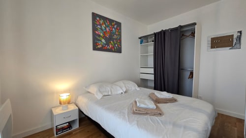 Bright bedroom in Ô KASTEL apartment, La Fôret-Fouesnant, with white bed, black closet, and colorful wall art