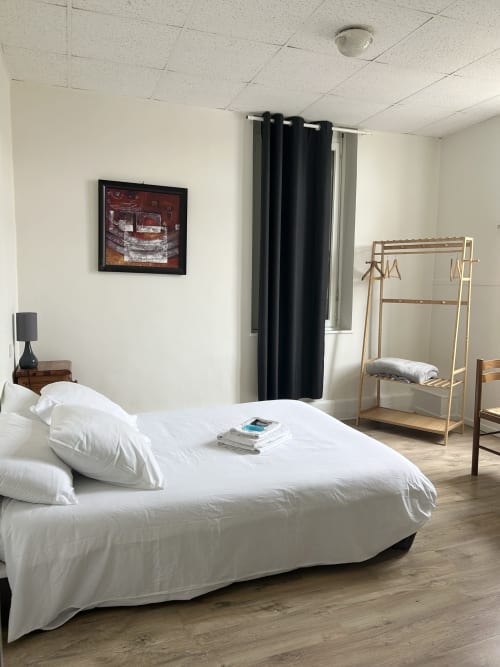 Chambre double lumineuse à l'hôtel BDM à Montastruc-la-Conseillère avec lit blanc, portant en bois et vue sur la ville