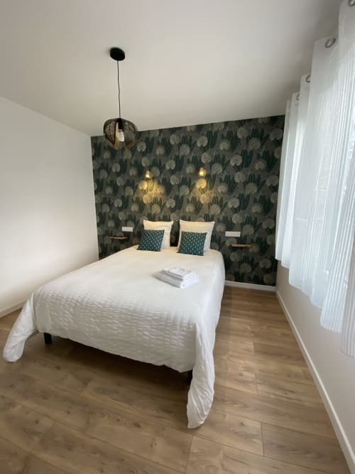 Chambre moderne dans l'appartement La Maison Blanche avec lit blanc, mur à motifs floraux, luminaires suspendus et parquet