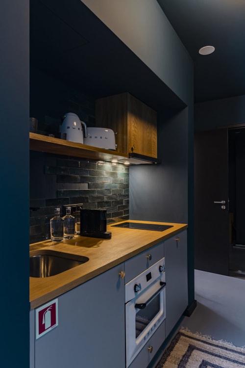 Kitchenette moderna em estúdio de hotel no Porto com bancadas de madeira, painel de azulejos escuros e eletrodomésticos de aço inoxidável