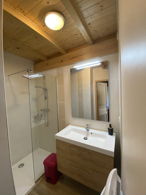 Salle de bain moderne du gîte Le Cocon De Curson avec douche ouverte, meuble-lavabo en bois, miroir et poutres en bois