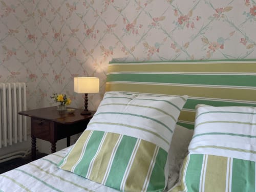 Chambre au Château de Vaux Morvan avec papier peint floral, literie rayée, table de nuit en bois foncé et lampe donnant sur le jardin